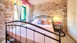 A bedroom with a stone wall, a bed with a metal frame, a bedside table with a candle, and a wardrobe. - Villa Kate (Kvarner - Čižići) (Čižići)