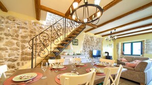 A dining area with a wooden table set for four, surrounded by white chairs. A stone wall and a wooden staircase with a wrought iron railing are visible. - Villa Kate (Kvarner - Čižići) (Čižići)