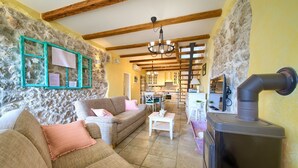 A cozy living room with a stone wall, wooden beams, a fireplace, and a kitchen in the background. - Villa Kate (Kvarner - Čižići) (Čižići)