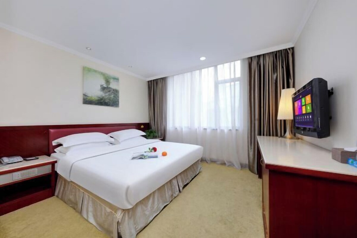 A hotel room with a bed, a desk, a television, and a window with curtains.