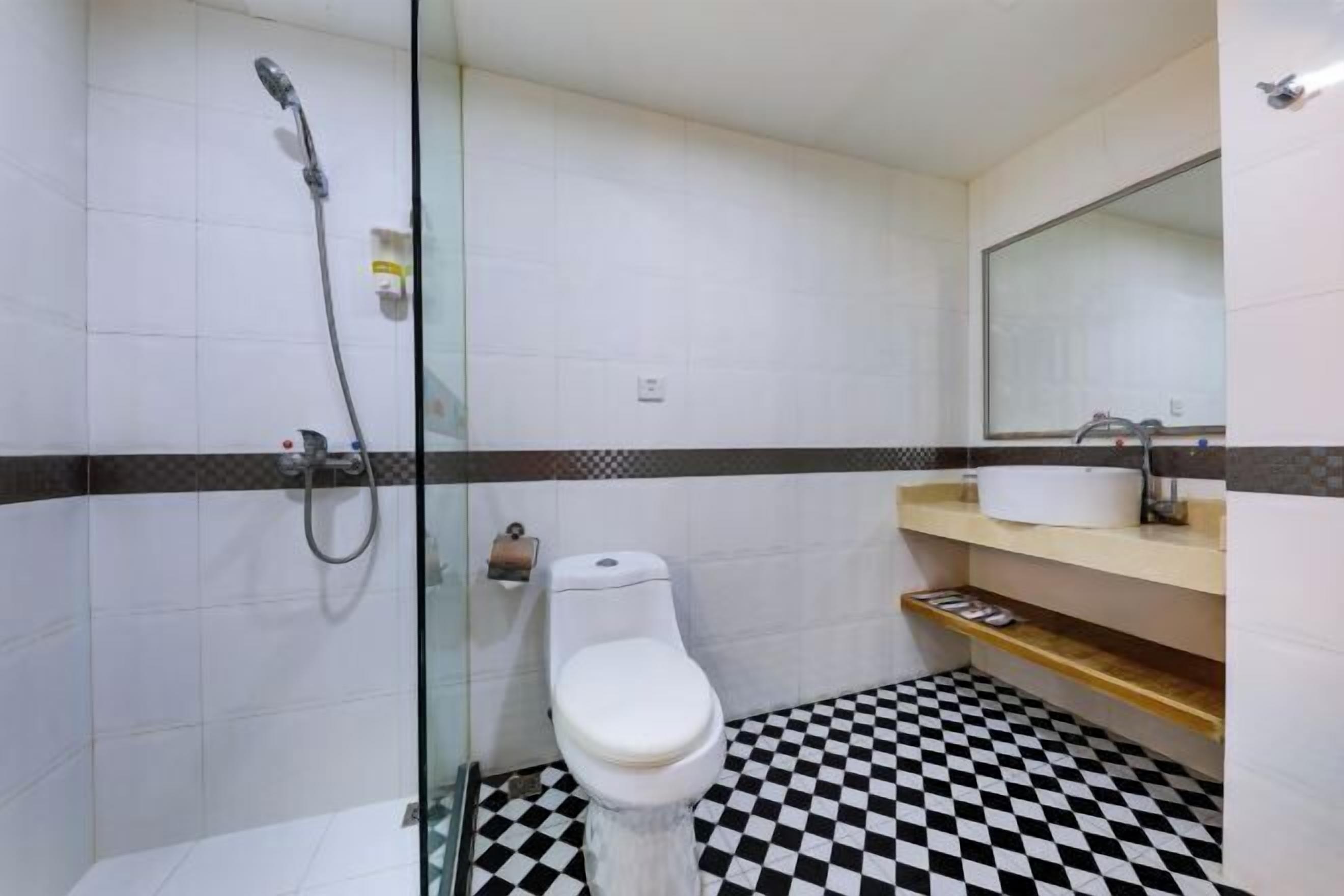 Casa de banho com cabine de chuveiro em vidro, sanita branca, lavatório com espelho e chão xadrez.