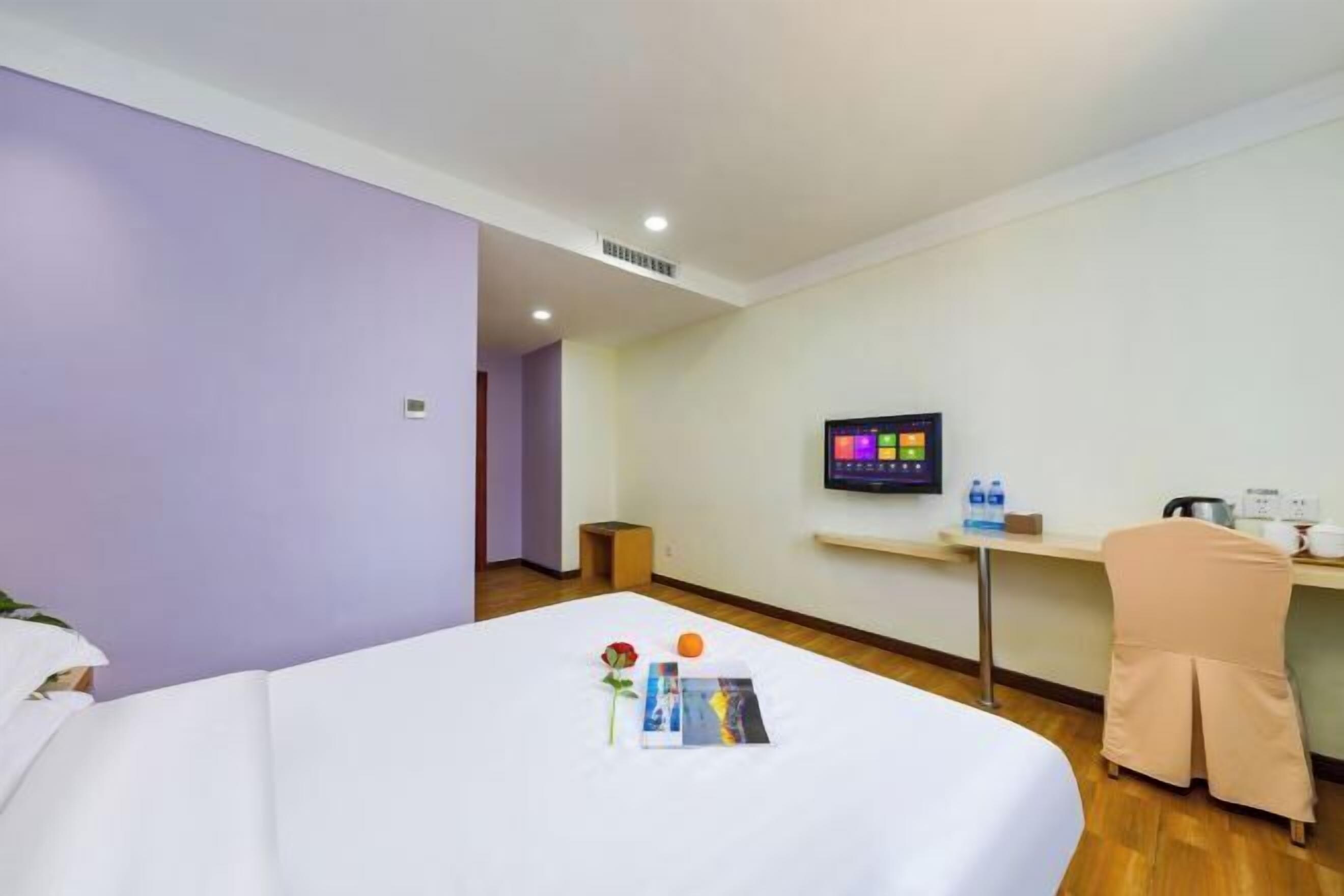 Habitación de hotel con cama, escritorio, televisor y una pequeña mesa con una botella de agua y una taza.