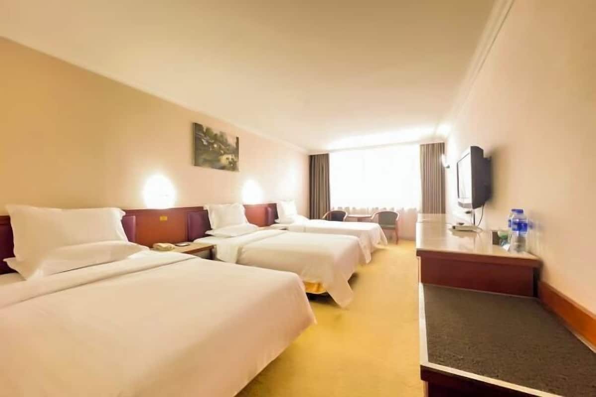 Habitación de hotel con tres camas, un escritorio, un televisor y una ventana con cortinas.