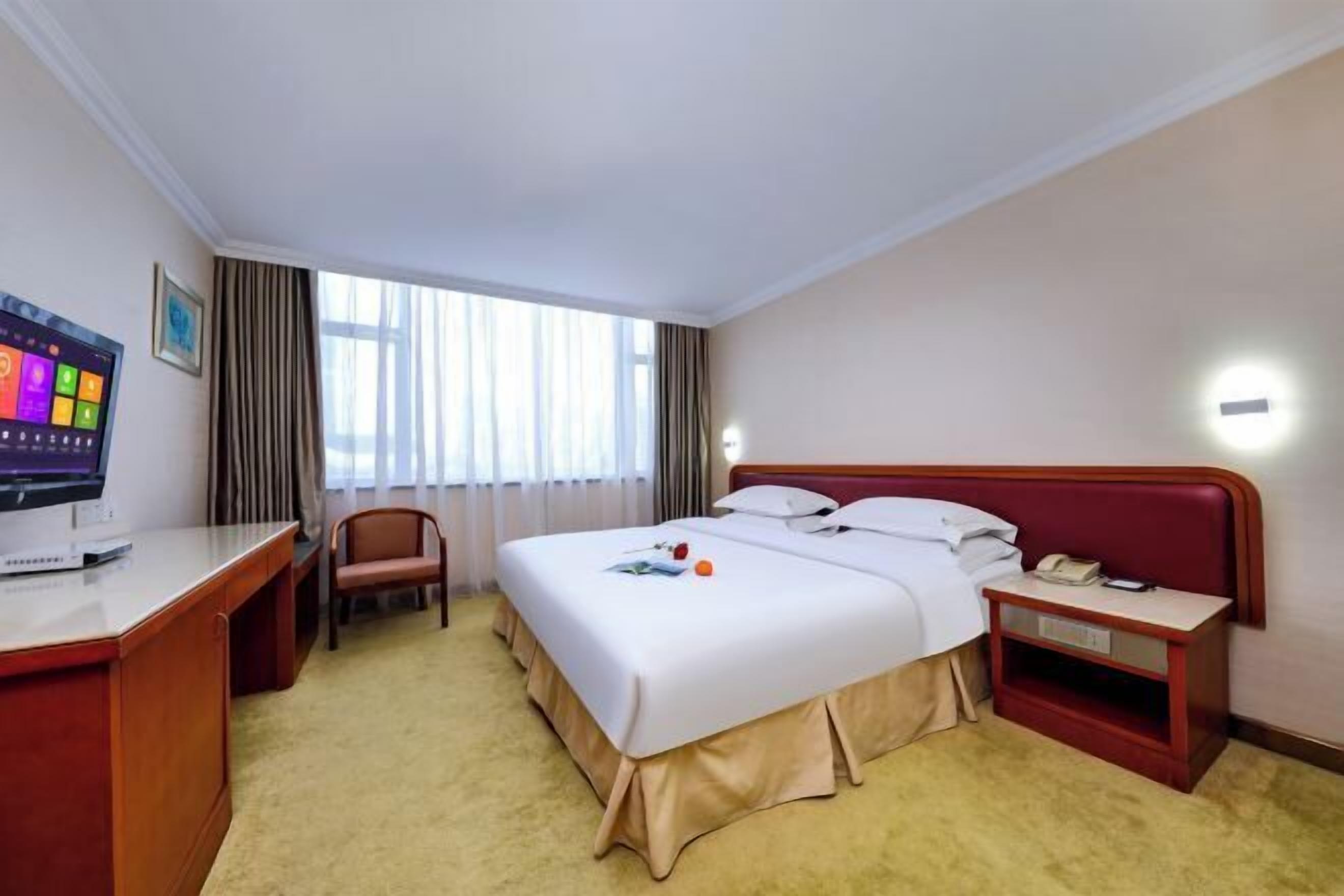 A hotel room with a bed, a desk, a chair, a TV, and a window with curtains.