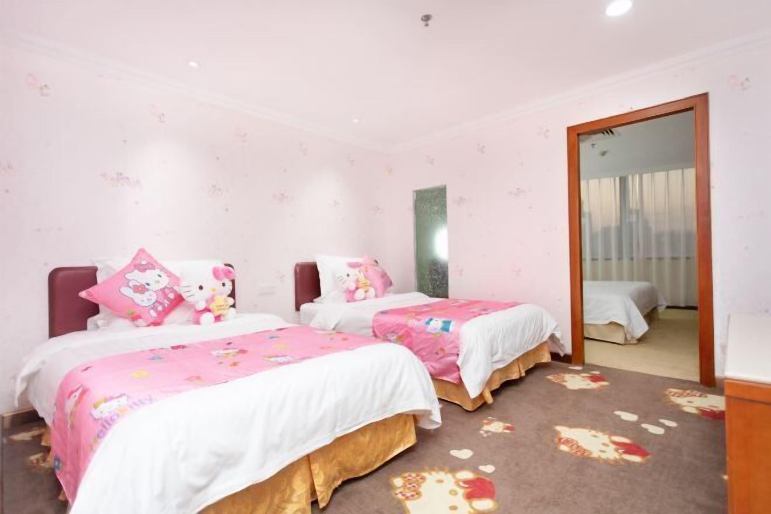 A bedroom with two beds, each with pink bedding and Hello Kitty pillows. The room has a carpet with a floral pattern and a mirror on the wall.