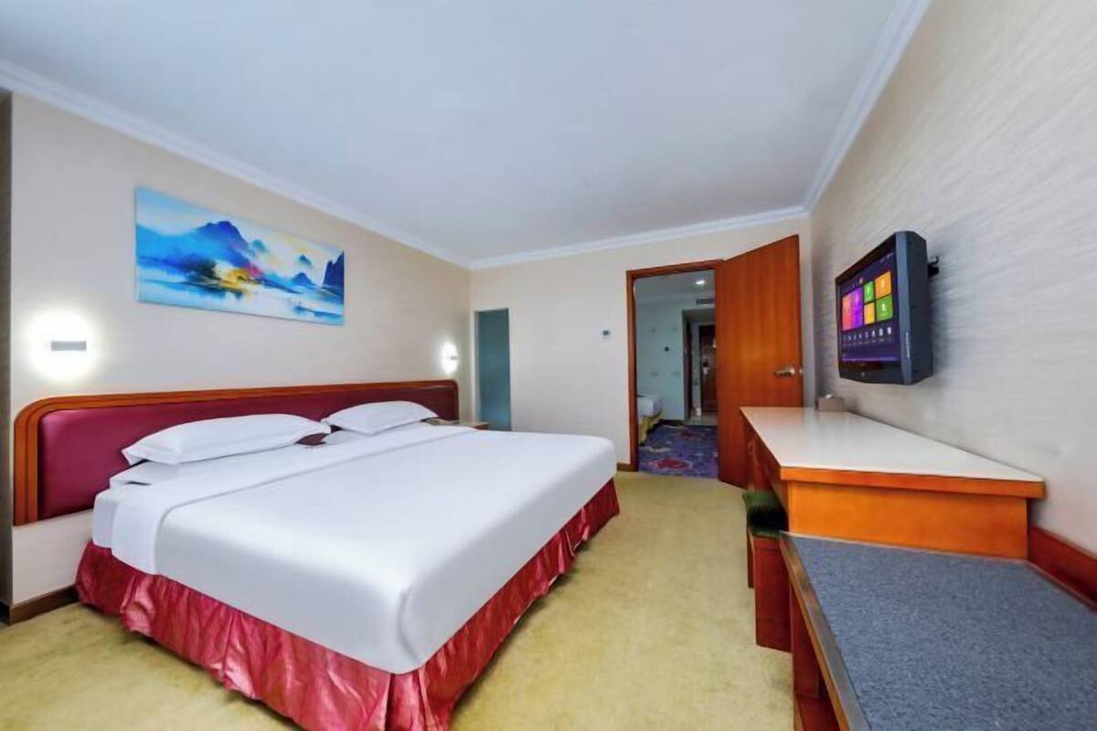 Habitación de hotel con cama, escritorio, televisor y un cuadro en la pared.