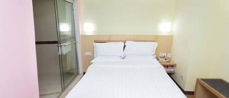 A hotel room with a bed, bedside table, and a glass door leading to a bathroom.