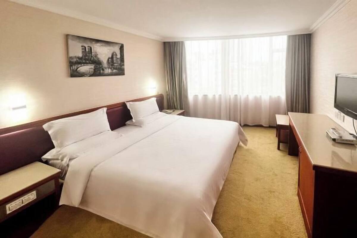 Una habitación de hotel con una cama grande, un escritorio, un televisor y un cuadro en la pared.
