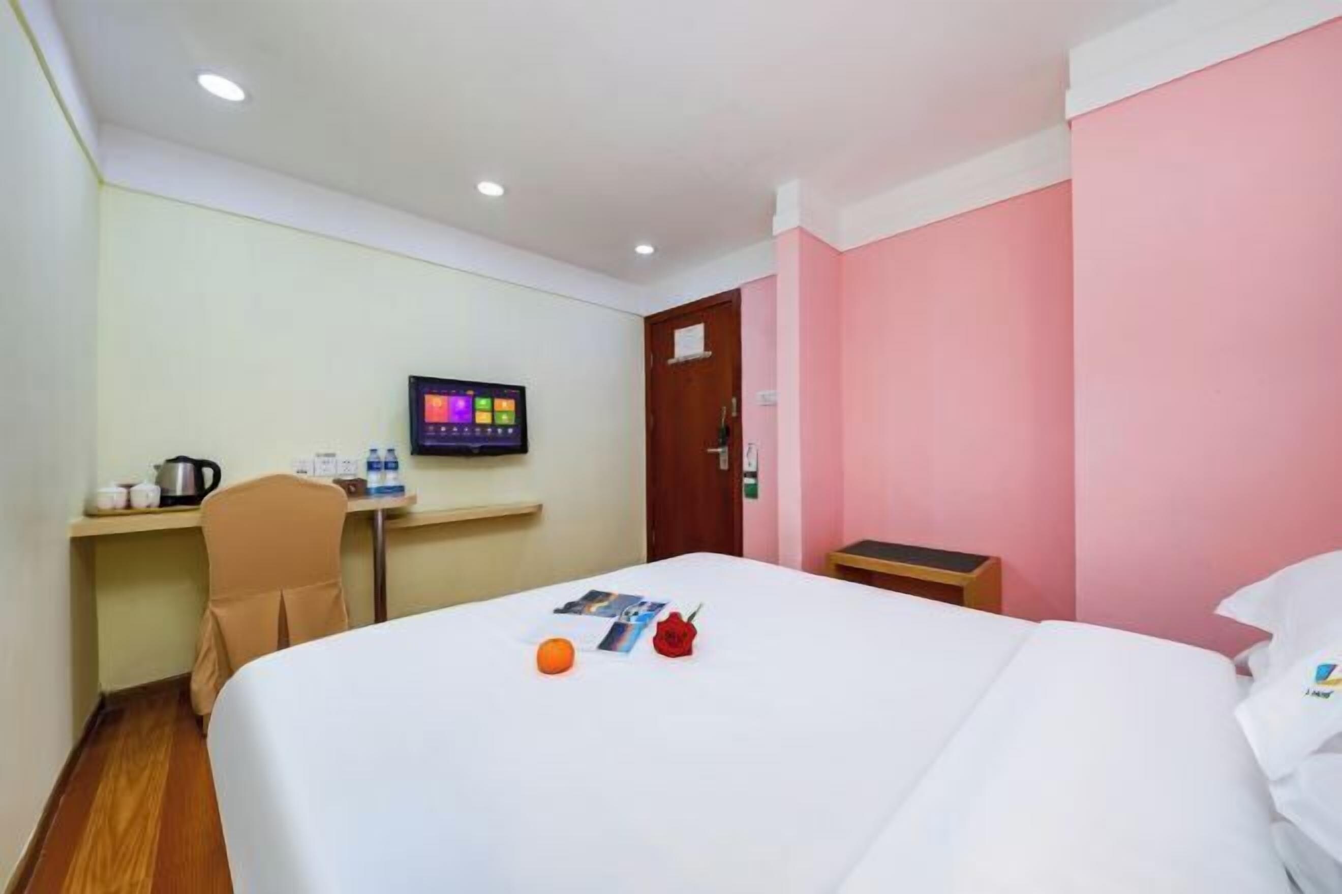 A hotel room with a bed, a desk with a computer monitor, a chair, and a small table.