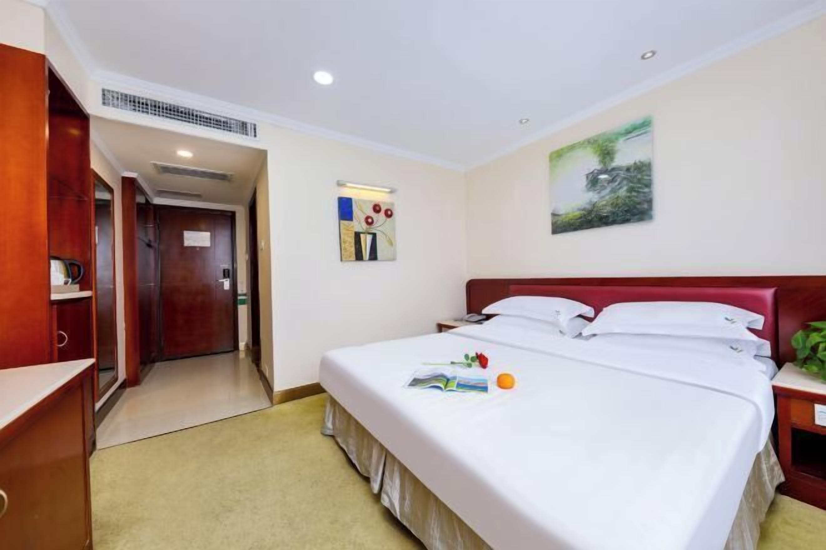 A hotel room with a bed, bedside table, and a painting on the wall.