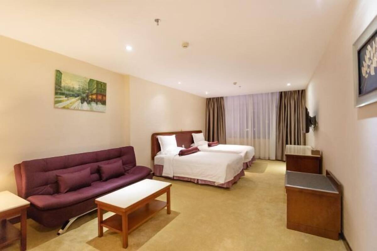 Habitación de hotel con sofá, dos camas individuales, escritorio y un cuadro en la pared.