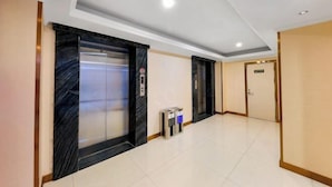 A hallway with two elevators, a trash bin, and a door. - L Hotel Zhuhai Gongbei Port Qinglv Road (Zhuhai)