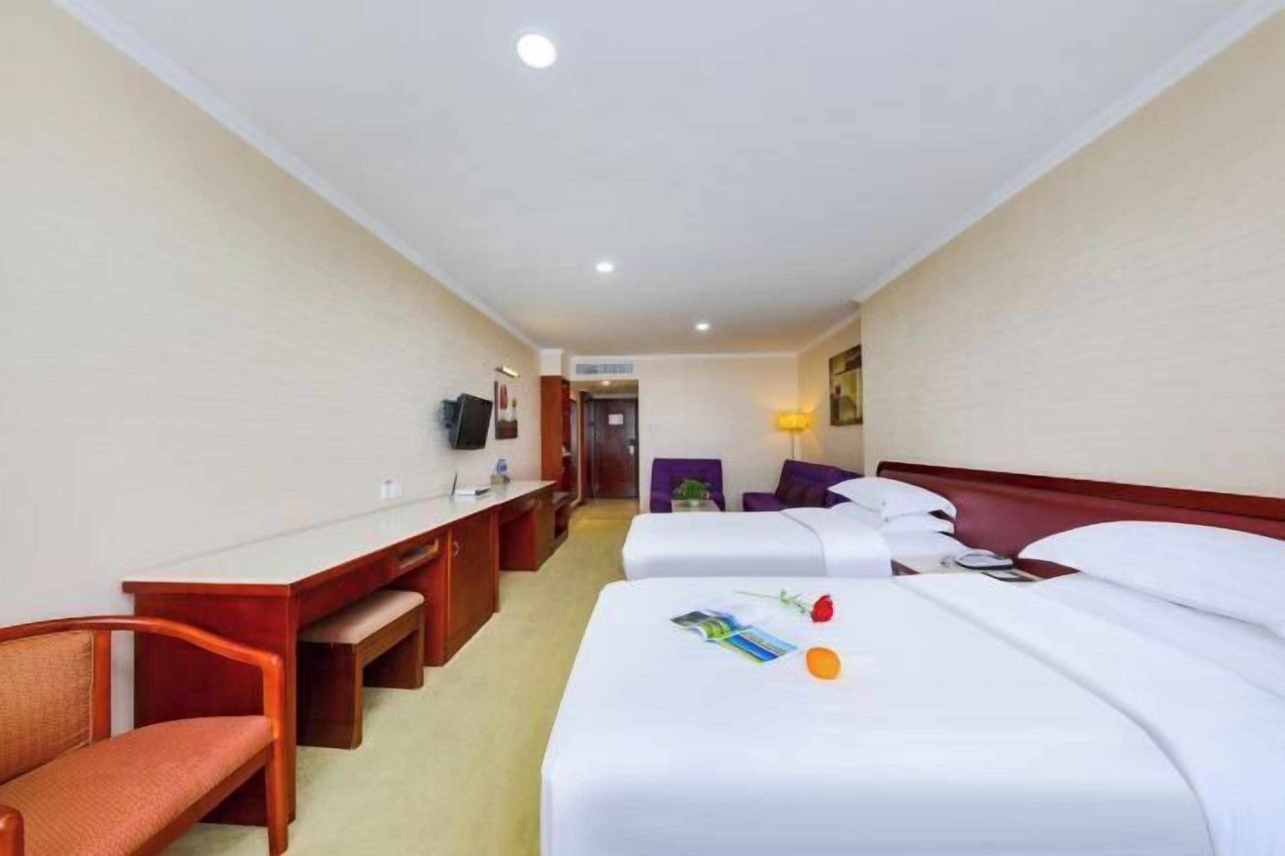 Habitación de hotel con dos camas, un escritorio, una silla y un televisor.