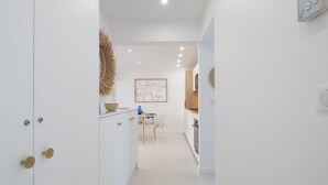 A modern kitchen with white cabinets, a dining area with a table and chairs, and a hallway leading to another room. - Stylish 2-Br Apartment Steps from the Croisette (Cannes)