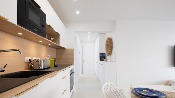 A modern kitchen with a microwave, toaster, and sink. There is a dining area with a table and chairs. - Stylish 2-Br Apartment Steps from the Croisette (Cannes)
