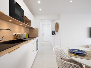 Een moderne keuken met een magnetron, broodrooster en spoelbak. Er is een eethoek met een tafel en stoelen.