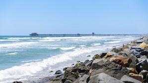 Una costa rocosa con olas rompiendo sobre la playa y un muelle que se adentra en el océano.