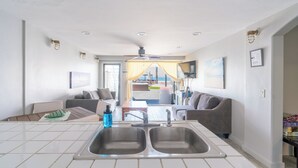 Una cocina moderna con un lavamanos doble, un comedor con mesa y sillas, y vistas a la playa a través de un ventanal grande.