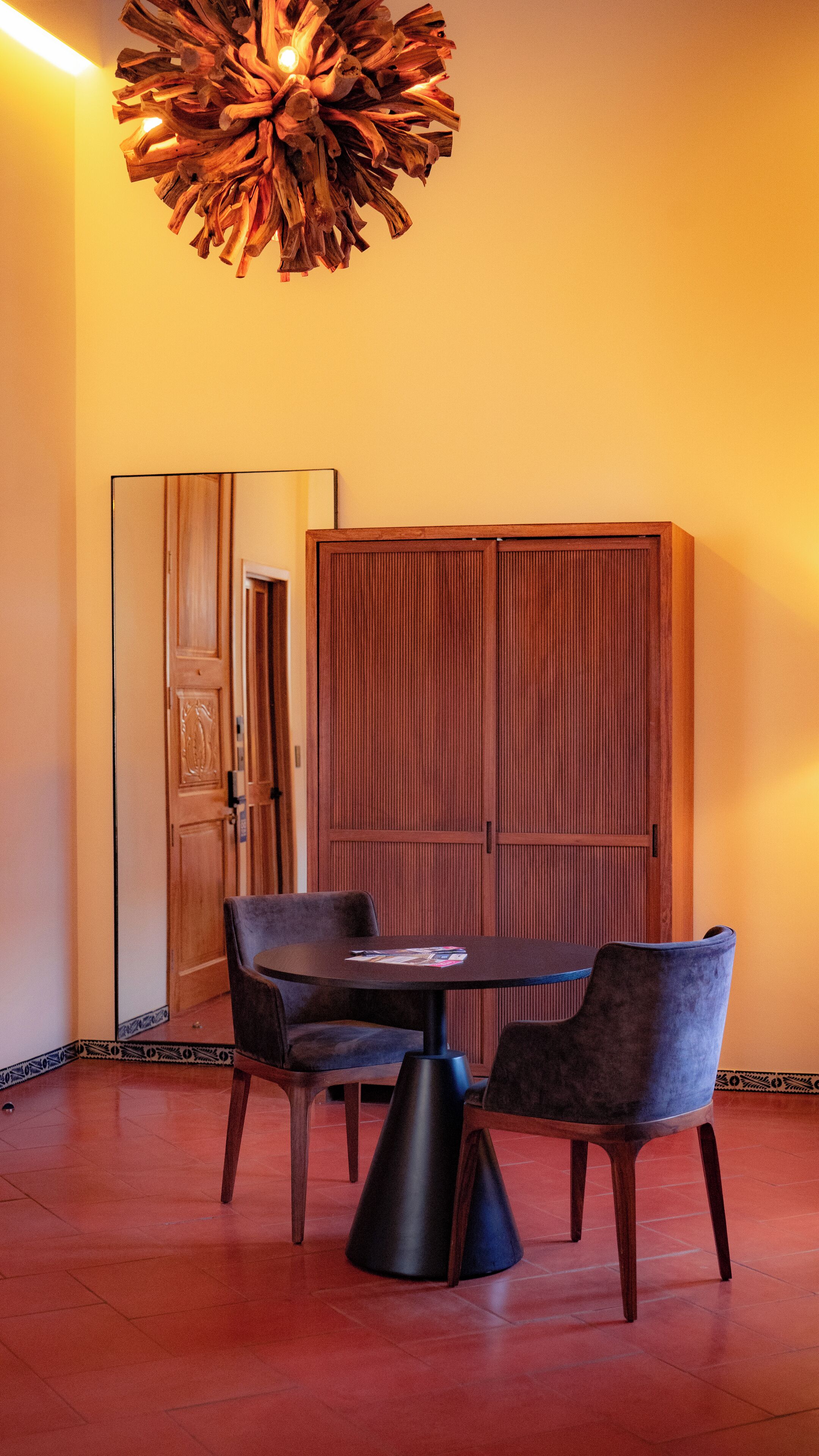 Uma sala de jantar com uma mesa redonda, duas cadeiras, um armário de madeira e um lustre de design exclusivo.