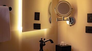 A bathroom with a large mirror, a round mirror, a black faucet, a wooden bowl sink, and a towel rack with towels.
