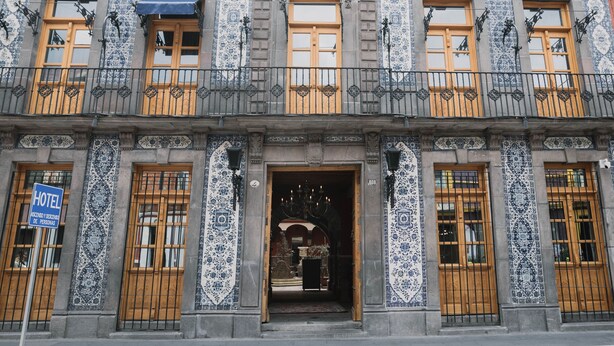 A hotel facade with ornate blue and white tile patterns, wooden doors, and a balcony with wrought iron railings. - Casa Azulai Puebla Hotel Boutique (Puebla)
