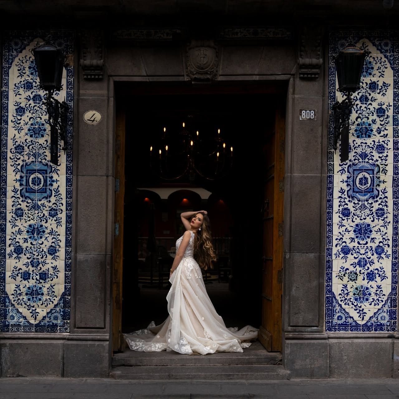 Una persona con un vestido de novia parada en la entrada de un edificio con baldosas de diseño azul y blanco.