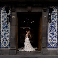 Una persona con un vestido de novia parada en la entrada de un edificio con baldosas de diseño azul y blanco.