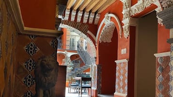 An interior with a staircase leading to an upper level, ornate columns, and a lion statue.