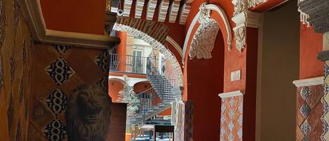 An interior with a staircase leading to an upper level, ornate columns, and a lion statue.