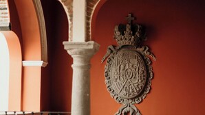 A room with a large coat of arms on the wall, a wooden chair, and a stone pillar.
