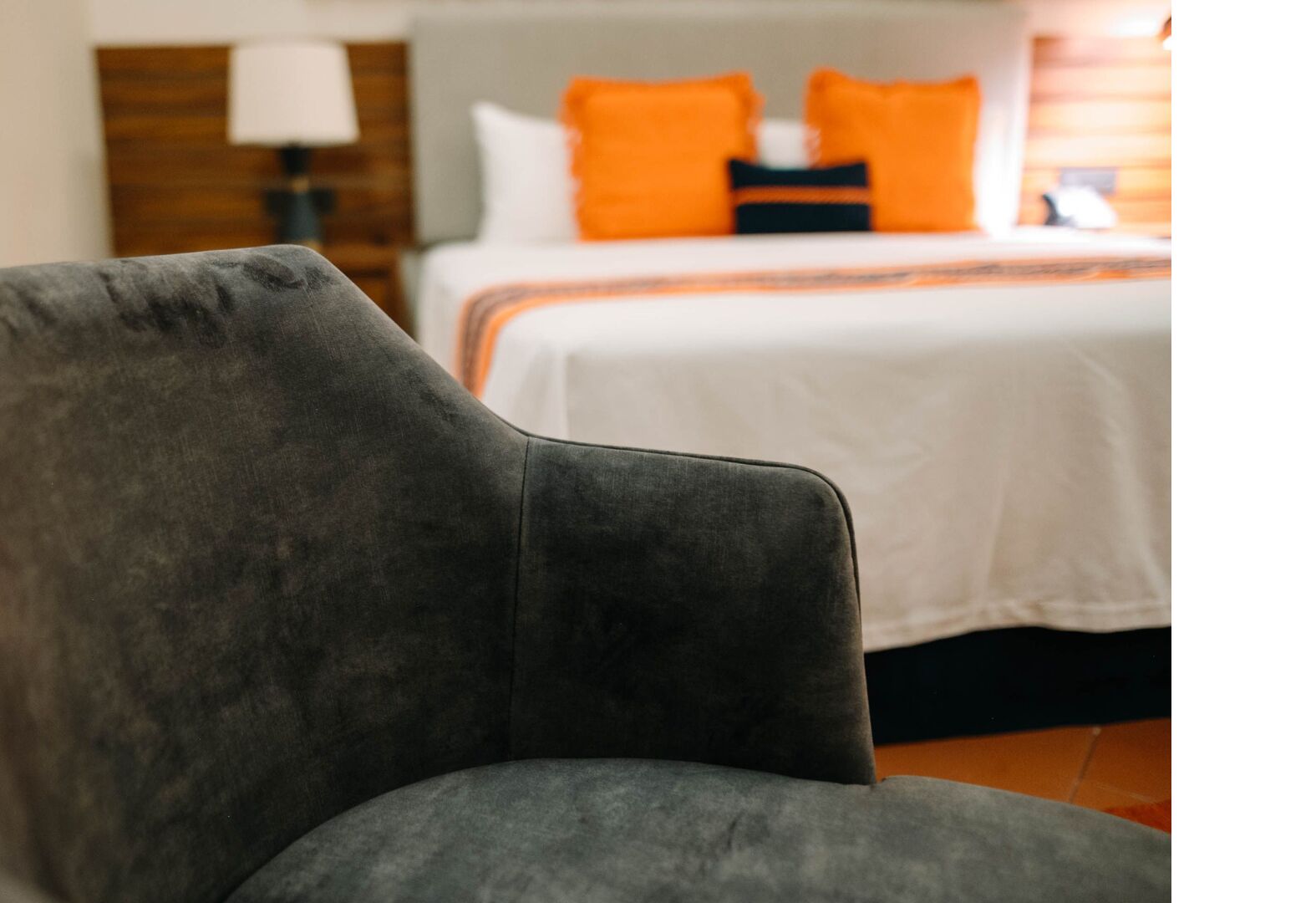 A grey armchair in a hotel room with a bed in the background.