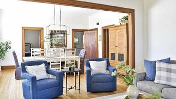 A spacious living room with a wooden ceiling, a dining area with white chairs, and a large wooden wardrobe.