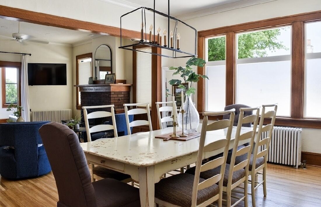 A dining area with a white table, wooden chairs, and a hanging light fixture.