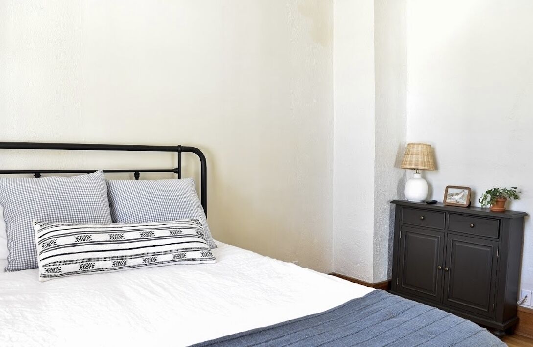 A bed with patterned pillows, a bedside table with a lamp, and a dark wooden cabinet.