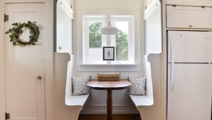 Eine Küche mit einem weißen Kühlschrank, einem Fenster mit Bilderrahmen und einer Bank mit Kissen.