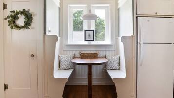 A kitchen with a white refrigerator, a window with a picture frame, and a bench with cushions.