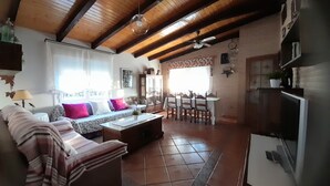 A spacious living room with a wooden ceiling, a sofa set, a dining table, and a kitchen area.