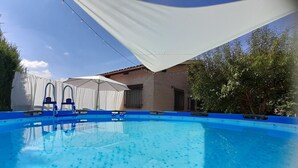 A swimming pool with a blue edge, surrounded by a white canopy and a brick building.