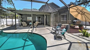 A backyard with a swimming pool, outdoor seating, and a covered patio area.