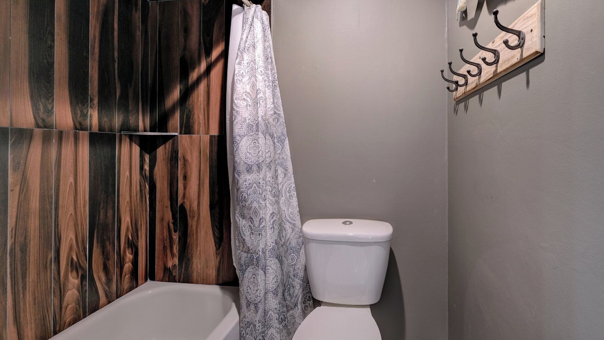 Un baño con pared de paneles de madera, inodoro blanco y cortina de ducha estampada.