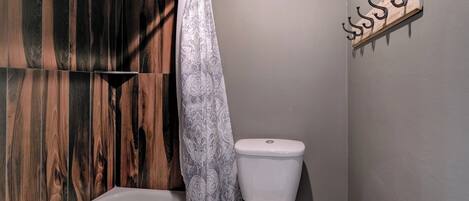 Un baño con pared de paneles de madera, inodoro blanco y cortina de ducha estampada.