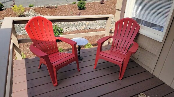 Deux chaises Adirondack rouges sont placées sur une terrasse en bois, avec une petite table ronde entre elles.