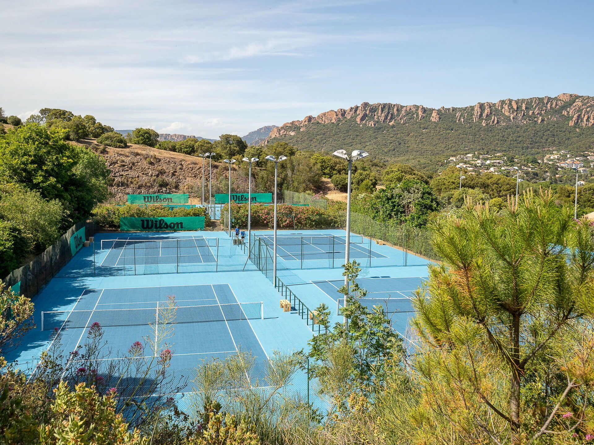Tennisbane omgivet af grøn vegetation og bjerge.