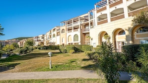 Um hotel com vários andares, varandas, um jardim bem cuidado e um céu azul límpido.