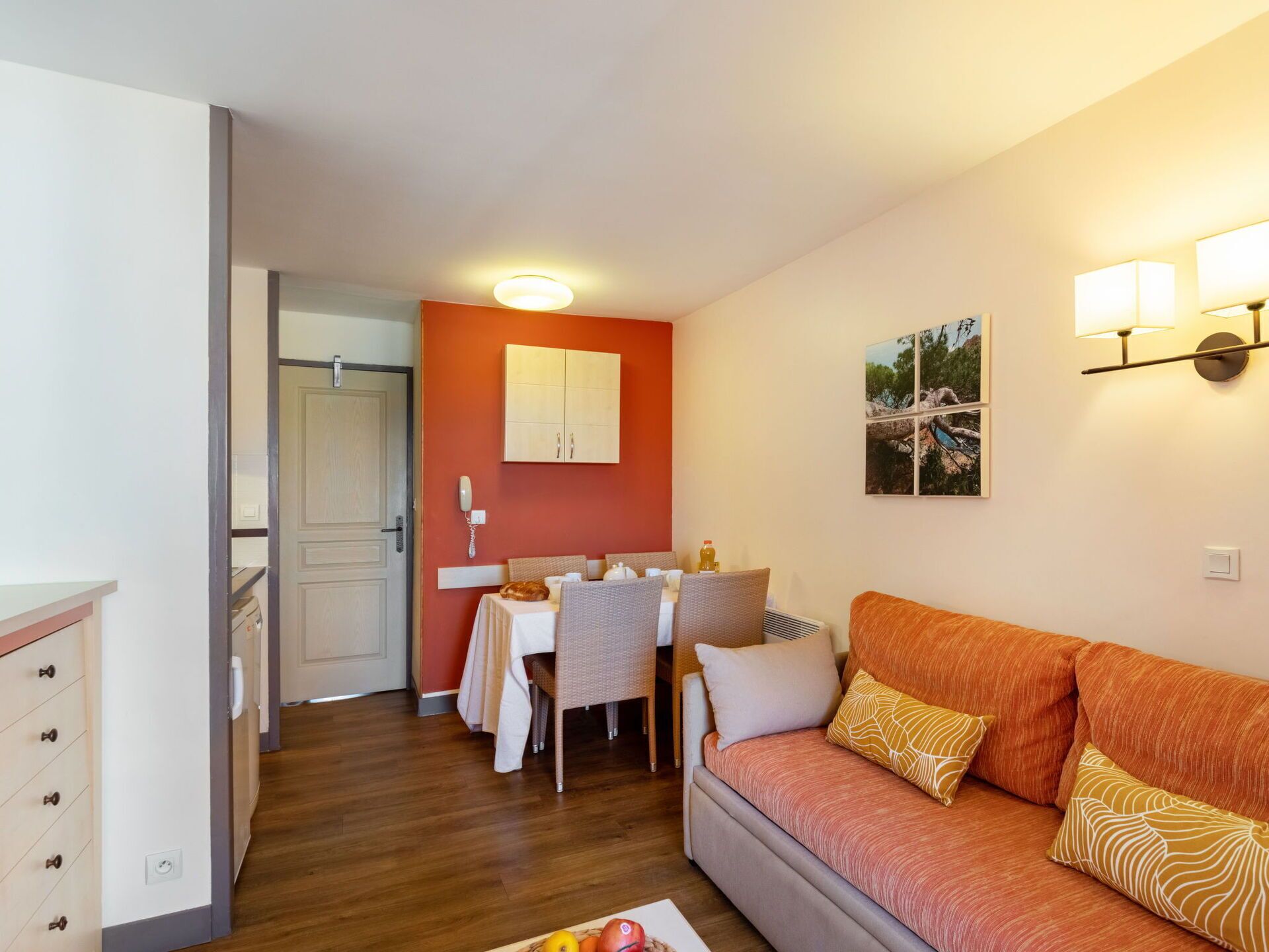 Un espacio habitable compacto con comedor, sofá, un mueble y una lámpara fijada a la pared.