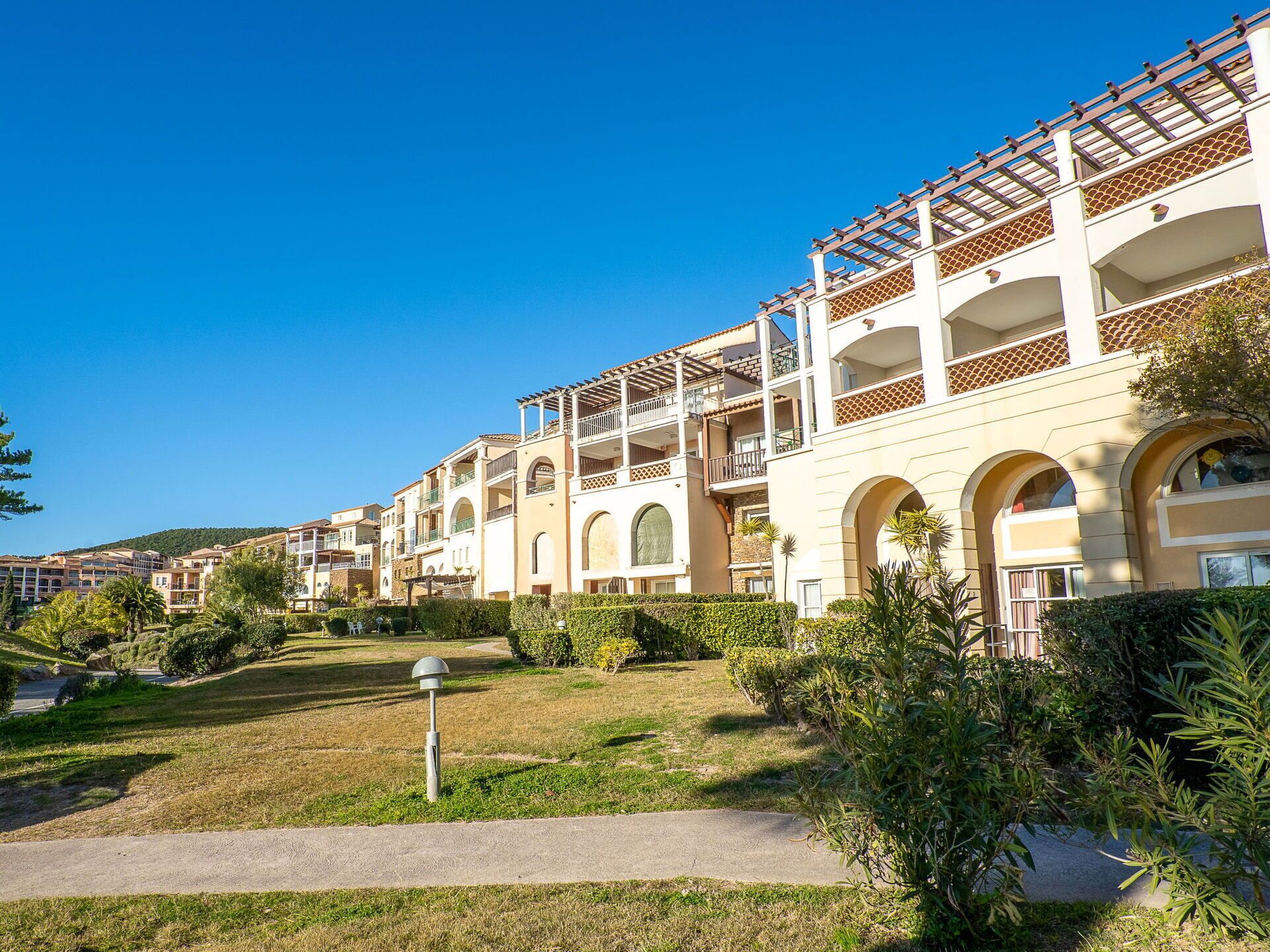 A multi-story hotel with balconies, a landscaped garden, and a clear blue sky.