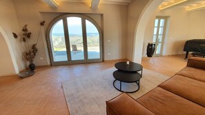 A spacious living room with a large sliding glass door leading to a patio, a black round table, and a brown leather sofa.