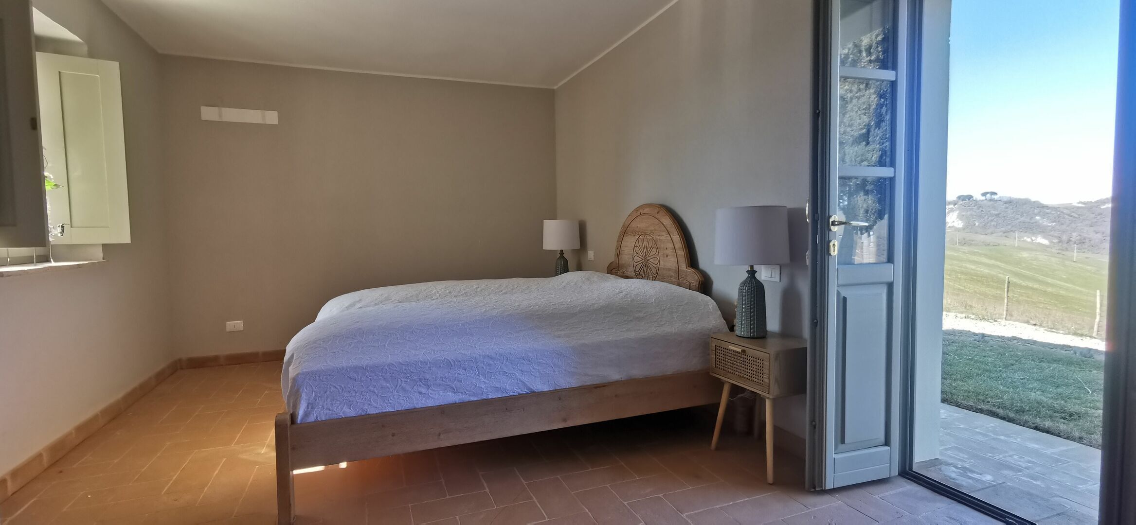 Un dormitorio con cama, mesita de noche, lámpara y puerta que da a un espacio exterior.
