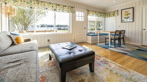 Una sala de estar con sofá, reposapiés y comedor con mesa y sillas.