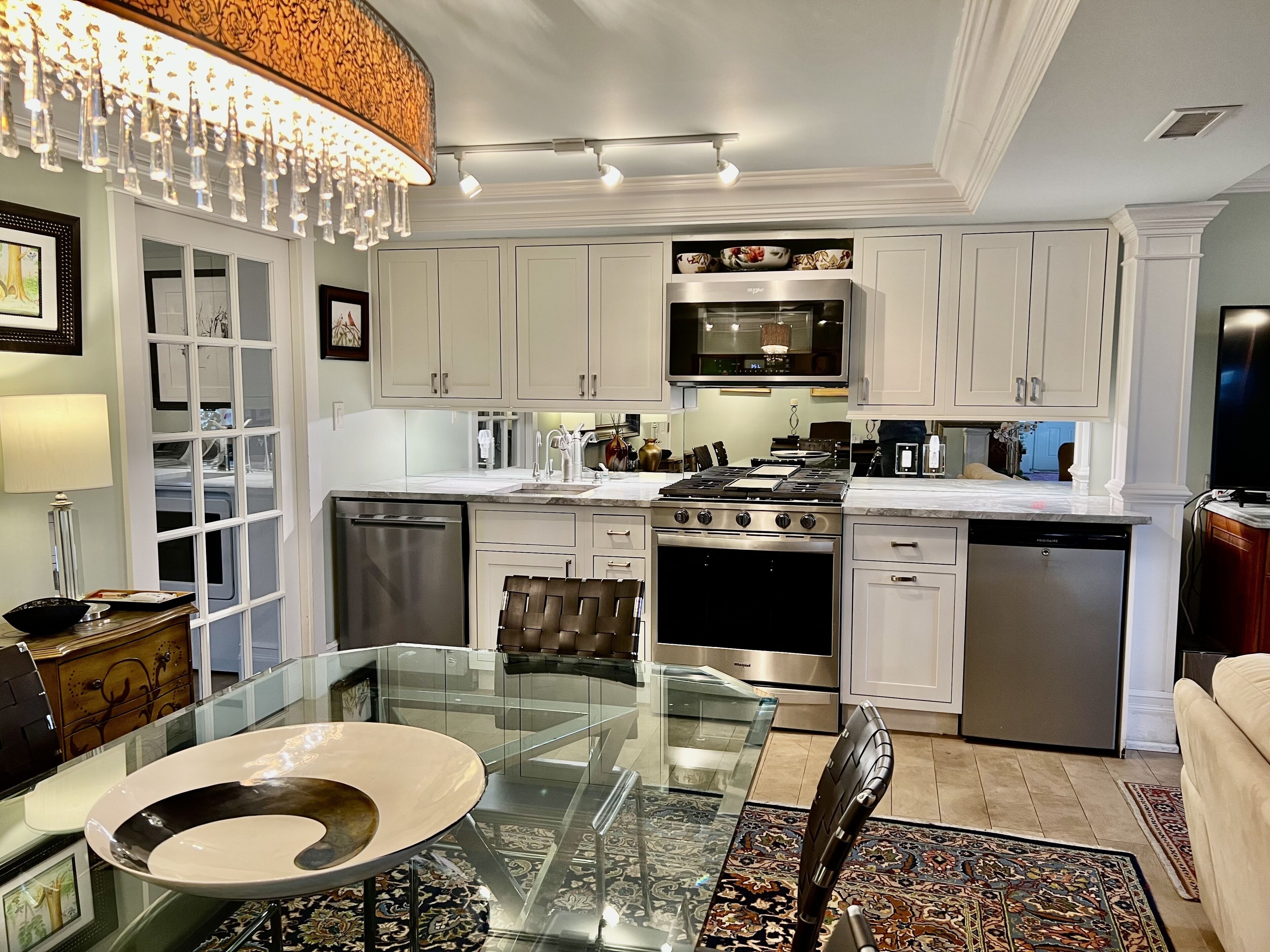 A modern kitchen with white cabinets, stainless steel appliances, and a glass dining table.